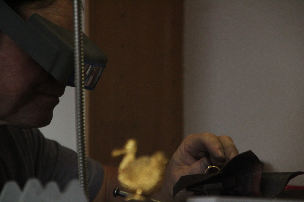 Der Goldschmied mit Lupenbrille bei der Arbeit, im Vordergrund eine kleine goldene Figur