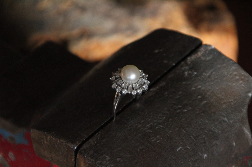 Ein Ring mit Perle und Diamantkranz in Weissgold ist im Schraubstock eingespannt