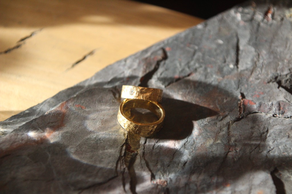 Zwei gehämmerte Eheringe aus Gelbgold liegen auf einem dunklen Stein im Streiflicht