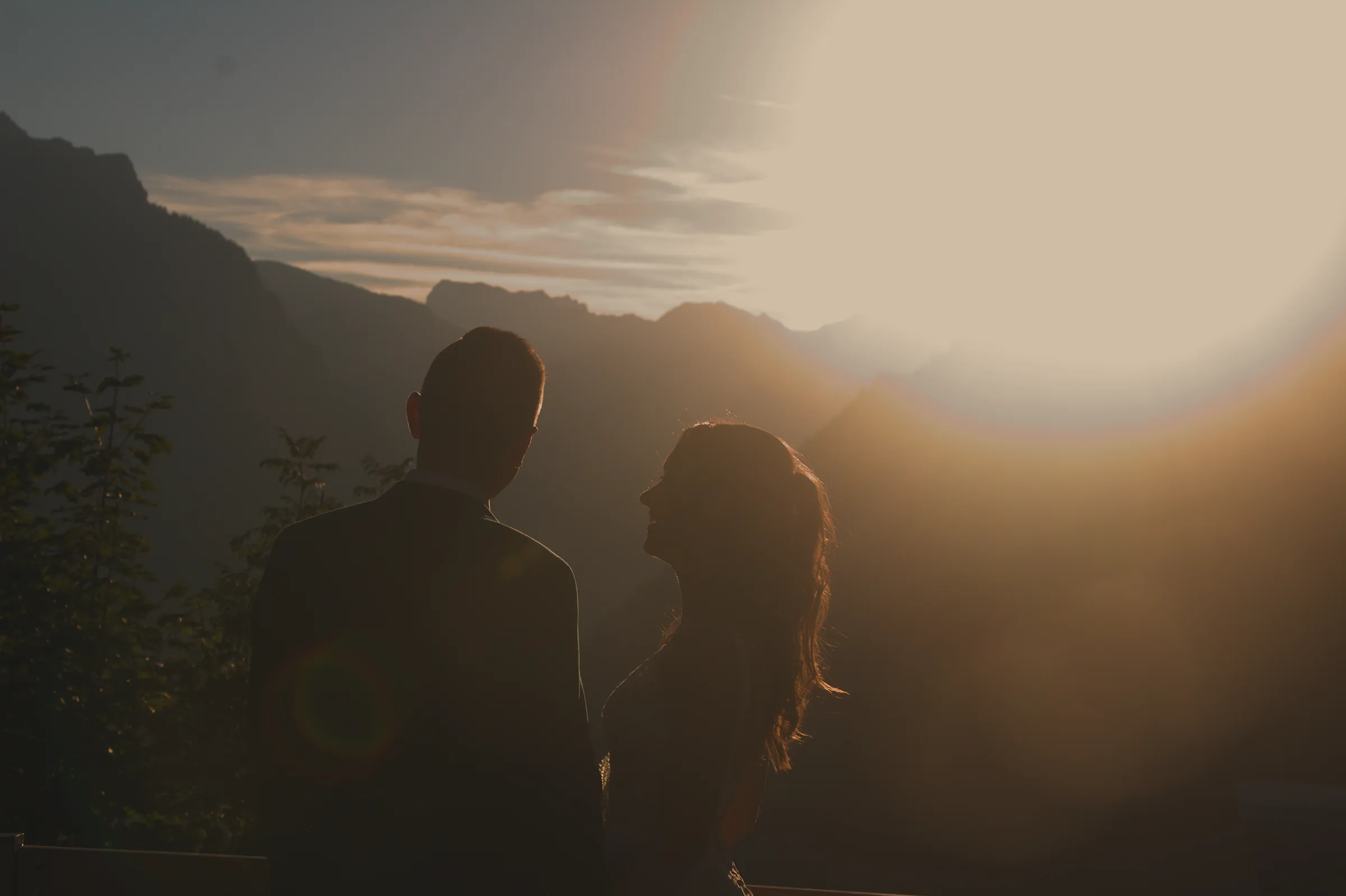 Brautpaar blickt im Gegenlicht der untergehenden Sonne in die Berge